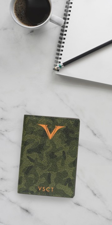 Camouflage passport holder on marble surface with notebook and cup of coffee