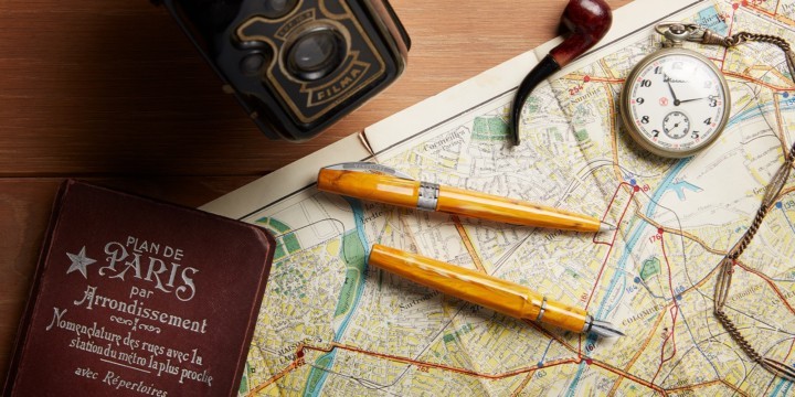 Amber-coloured Mirage fountain pen and rollerball pen on a yellow map, with an old fashioned camera, pipe and watch