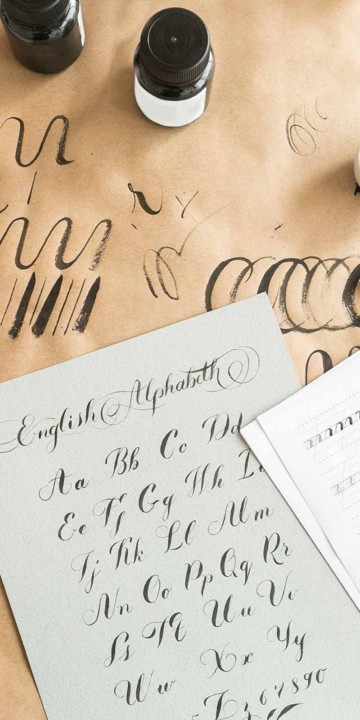 Calligraphy exercises on white, gray and yellow sheets of paper with ink bottles