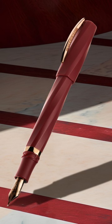 Visconti Divina Matte Bordeaux fountain pen with gold metalwork on a striped red and white background